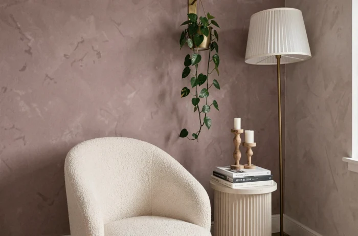 Coin lecture aménagé dans une chambre avec un fauteuil bouclé ivoire, une table d'appoint cannelée en plâtre et un mur en stuc chaulé rose mauve, décoré d'une plante pothos suspendue